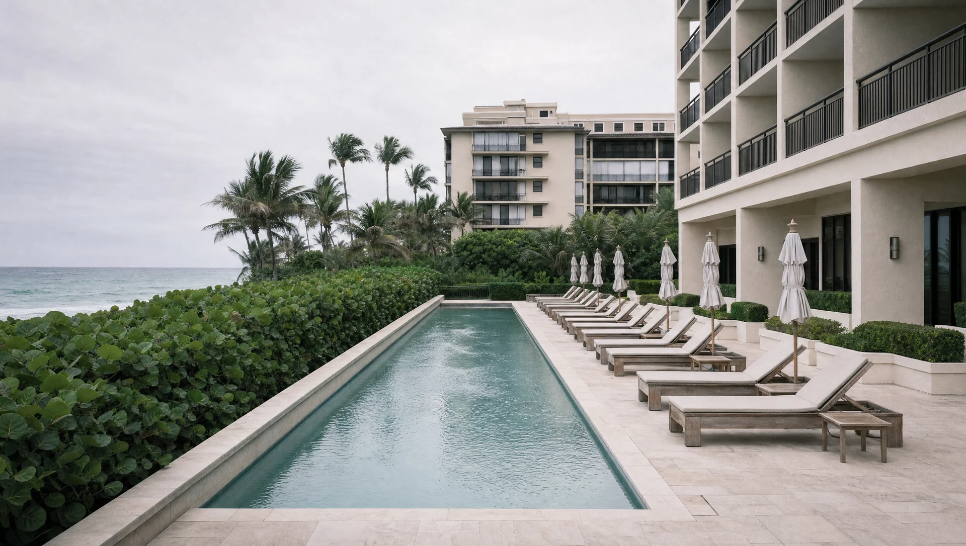 An empty pool terrace at a Palm Beach oceanfront condominium, loungers set out along the water.